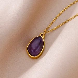Macro detail of a 18K gold plated necklace with a teardrop purple crystal on silk fabric