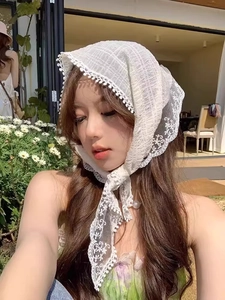 Close-up of white floral lace headscarf with small pom-pom trim on a model outdoors