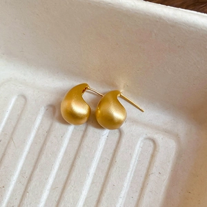 Macro detail of gold plated teardrop earrings with a brushed matte metallic finish