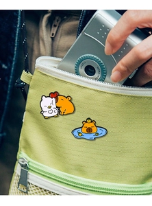 Detail of cute Capybara and crocodile enamel pins displayed on a green canvas bag