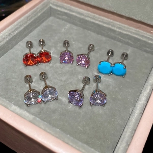Detailed view of five pairs of zircon stud earrings in various colors on grey velvet