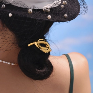 Elegant gold metal hair tie with twisted knot design worn on a stylish low bun