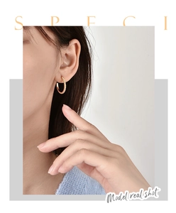 Detail of gold-plated spiral twist C-shaped hoop earrings on a model with metallic shine
