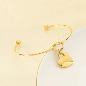 Close-up of a gold minimalist heart charm open bangle with detailed metallic texture