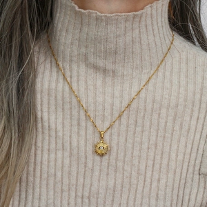 Golden sunburst evil eye necklace with zircon on beige knit sweater background