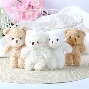 Set of four plush teddy bear charms in cream and brown with metal chains on a woven mat