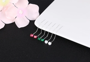Close-up of tassel earrings with red green and white cubic zirconia on white porcelain