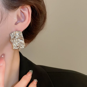 Close-up of model wearing silver crinkled rectangular stud earrings with metallic texture