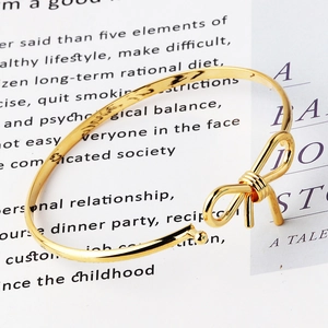 Elegante bracciale rigido dorato aperto con fiocco e design geometrico minimalista
