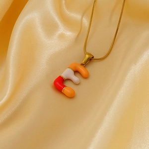 Collier chaîne serpent dorée avec pendentif lettre E en émail coloré sur satin jaune