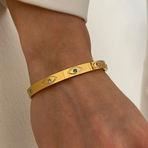 Brazalete de acero dorado con diseño de ojo y circonitas de colores en la muñeca
