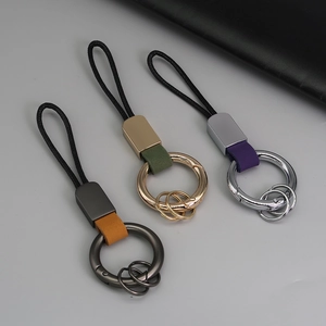Trois porte-clés en cuir tressé en marron, vert et violet avec anneaux métalliques