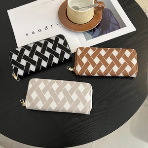 Three long woven wallets in black, brown, and white with elegant gold zippers on a table