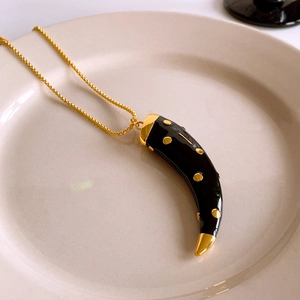 Detail of a vintage horn pendant necklace with black drip oil and gold metal accents