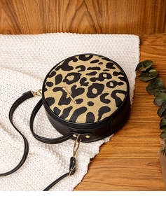 Detail of round leopard print crossbody bag on a white knit blanket with wooden background
