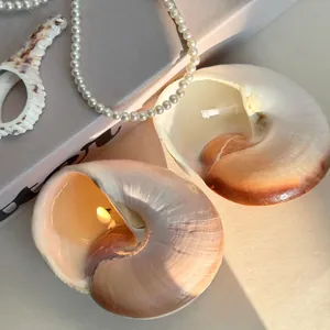 Detailed close-up of a lit conch shell scented candle with a warm glow and pearl accents