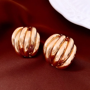 Détail de boucles d'oreilles dorées multicouches torsadées sur fond de soie rouge foncé