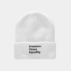 Close-up of white cuffed beanie featuring black Freedom Peace Equality text embroidery