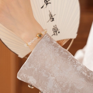 Detail of beaded white crystal bracelet with a golden hollow charm on a female wrist