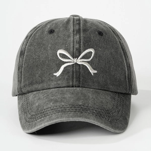 Detailed close-up of white bow embroidery on washed charcoal grey cotton baseball cap