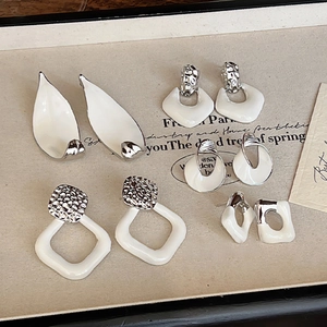 Close-up of assorted white enamel and silver geometric earrings on a vintage paper