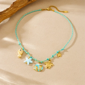 Golden sea turtle and shell pendants on blue woven cord necklace with beach background