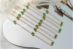 Close-up of square emerald zircon pendants on 18K gold plated chains with reflections