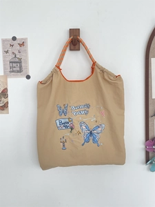 Detail of khaki canvas tote with blue butterfly embroidery and woven orange handle