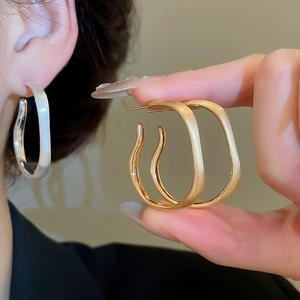 Detail of matte gold and silver wavy square hoop earrings shown on hand and ear