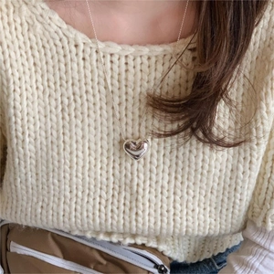 Detail of a 3D puffed heart pendant on a delicate ball chain against a beige sweater