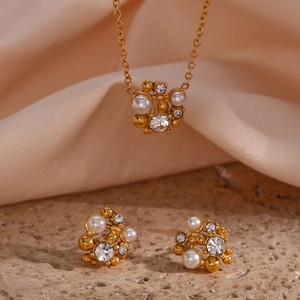 Golden 18K plated stainless steel jewelry set with pearls and rhinestones on stone background