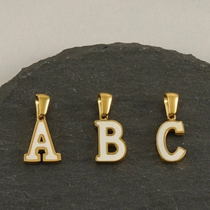 Détail de pendentifs lettres A B C dorés avec émail blanc posés sur une pierre d'ardoise