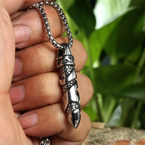 Macro shot of silver stainless steel dagger pendant with detailed scale textures held by hand
