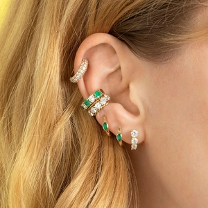 Vue macro détaillée de boucles d'oreilles dorées avec zircons verts et blancs sur l'oreille