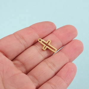 Close-up of small gold hollow cross pendant on a palm for size reference on blue background