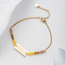 Macro shot of gold-plated chain with leaf engraved plaque and colorful gemstone beads
