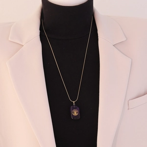 Detail of a square purple stone pendant featuring a golden tree of life on a long chain