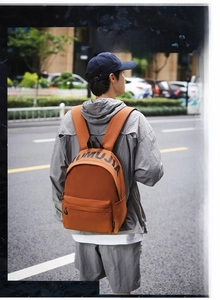 Street lifestyle shot of an orange-brown waterproof nylon backpack with UMUJIA lettering