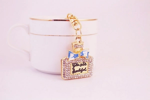 Detail eines Strass-Parfümflaschen-Schlüsselanhängers mit blauer Schleife an Teetasse