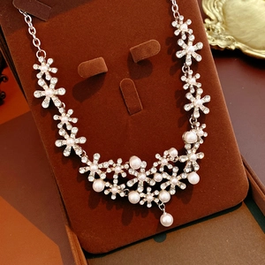 Close-up of floral crystal necklace with pearl pendant on brown velvet display