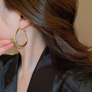 Macro shot of large golden water-drop earrings on a model showing polished metal finish