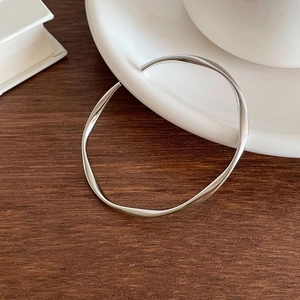 Detailed view of the twisted silver Mobius bangle on a rustic wooden texture