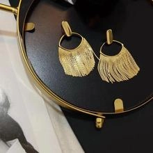 Detailed view of long gold tassel earrings with sleek fringe chains on a black tray