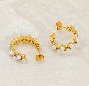 Macro shot of gold C-shaped earrings with pearls and white zircon stones in vintage style