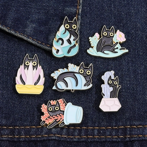 Detail of six creative black cat enamel pins on denim, showing cartoon animal designs