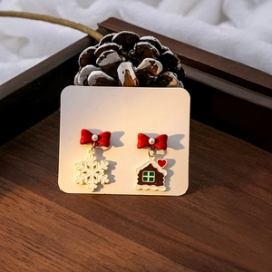 Boucles d'oreilles Noël asymétriques avec nœud rouge et flocon sur fond de pommes de pin