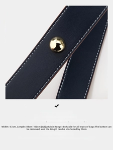 Detail of dark blue leather bag strap with white stitching and gold metal buckles