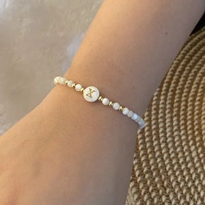 Macro shot of beaded shell bracelet with gold letter X charm worn on wrist