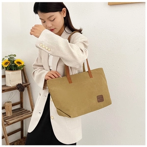 Close-up of large canvas tote bag showing the leather logo patch and brown handles