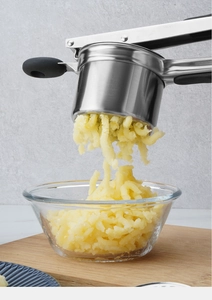Stainless steel potato ricer with silicone handles pressing mash into a glass bowl
